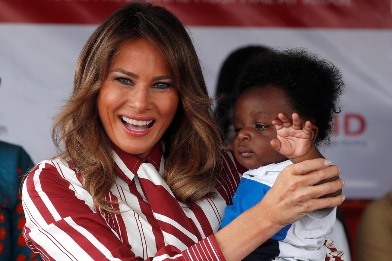 The photo shows the first lady in a red and white striped dress standing with the child. 
