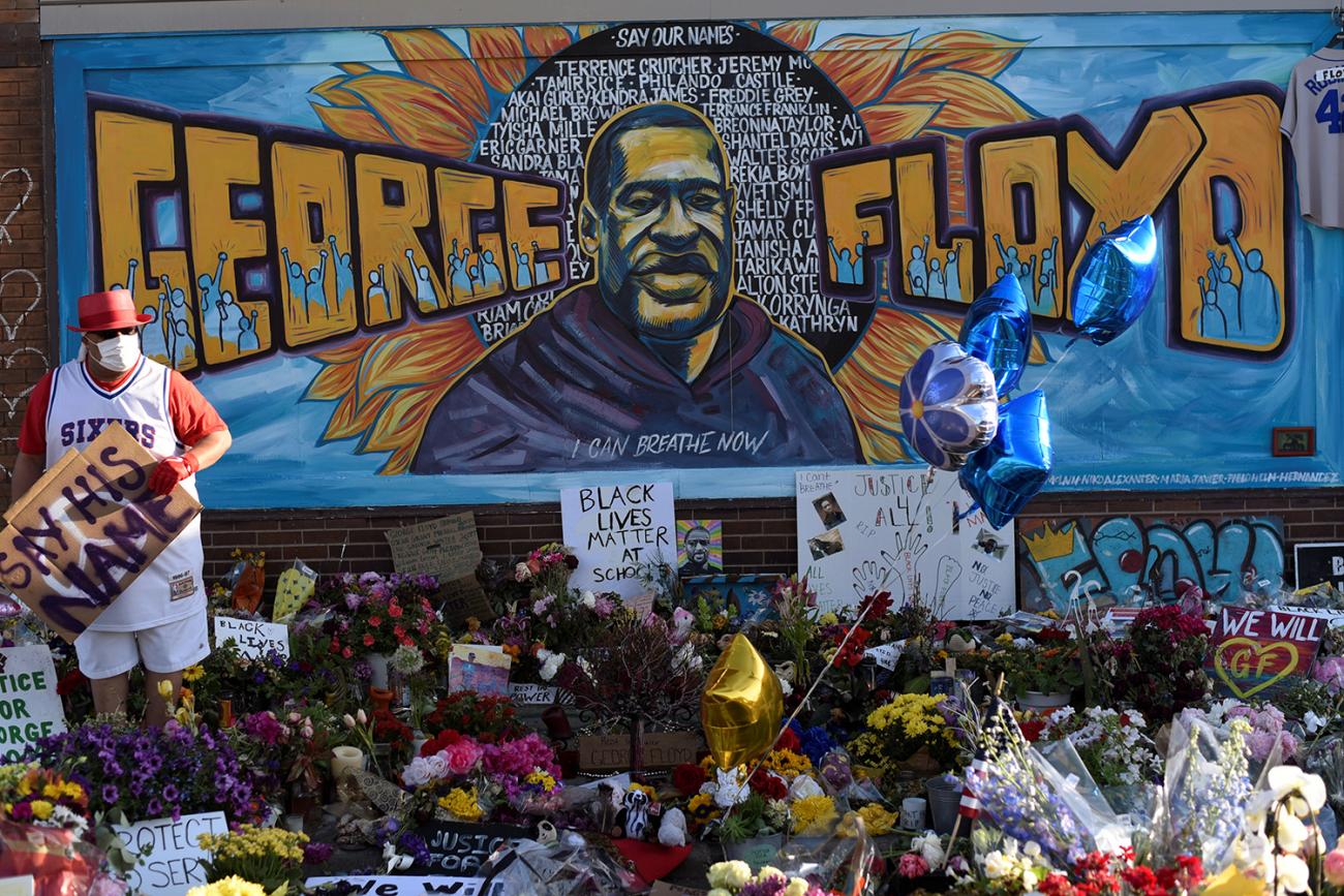 The photo shows a mural to Floyd with lots of flowers and signs laid out in front. 