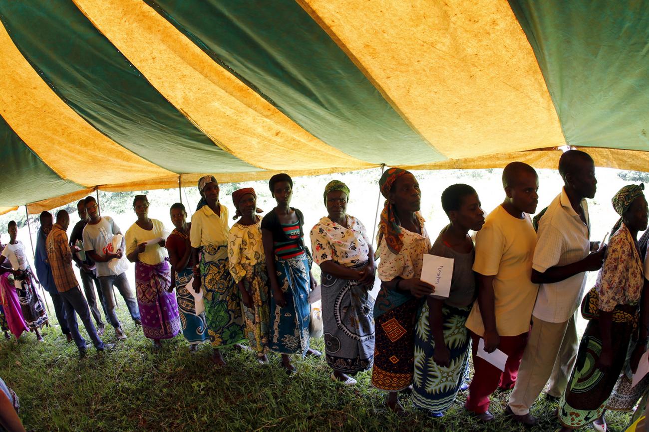 The photo shows people in a line under a green and yellow-striped tent. This is a striking image. 