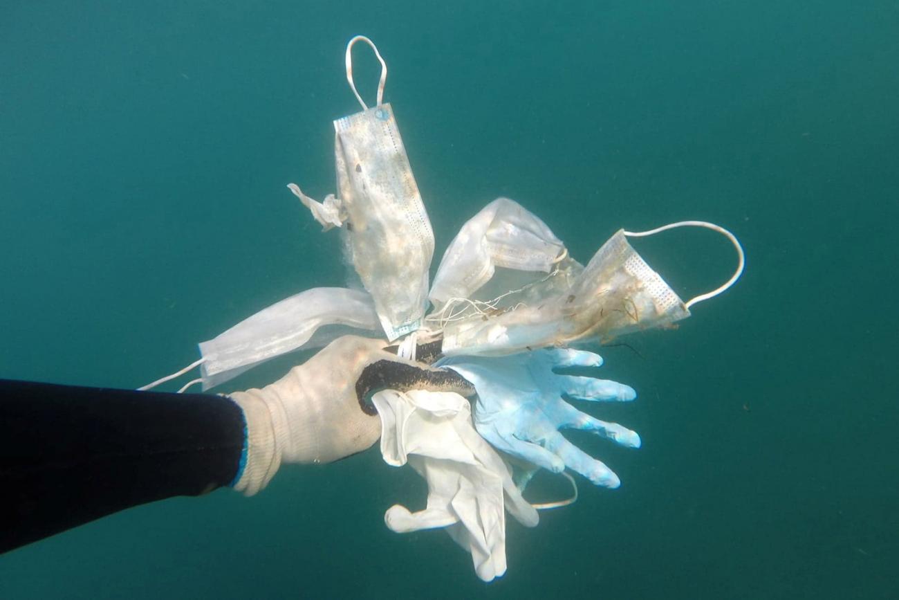 The photo shows a hand underwater holding a bunch of PPE. 