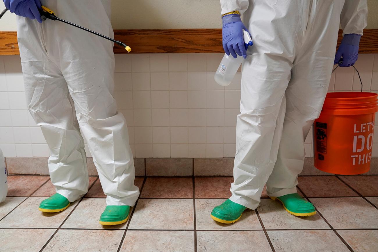Two torsos, two pairs of legs—bodies dressed in white protective suits—two pairs of green shoes, blue gloves, and two headless bodies, one holding a red bucket. That's what the picture shows. 