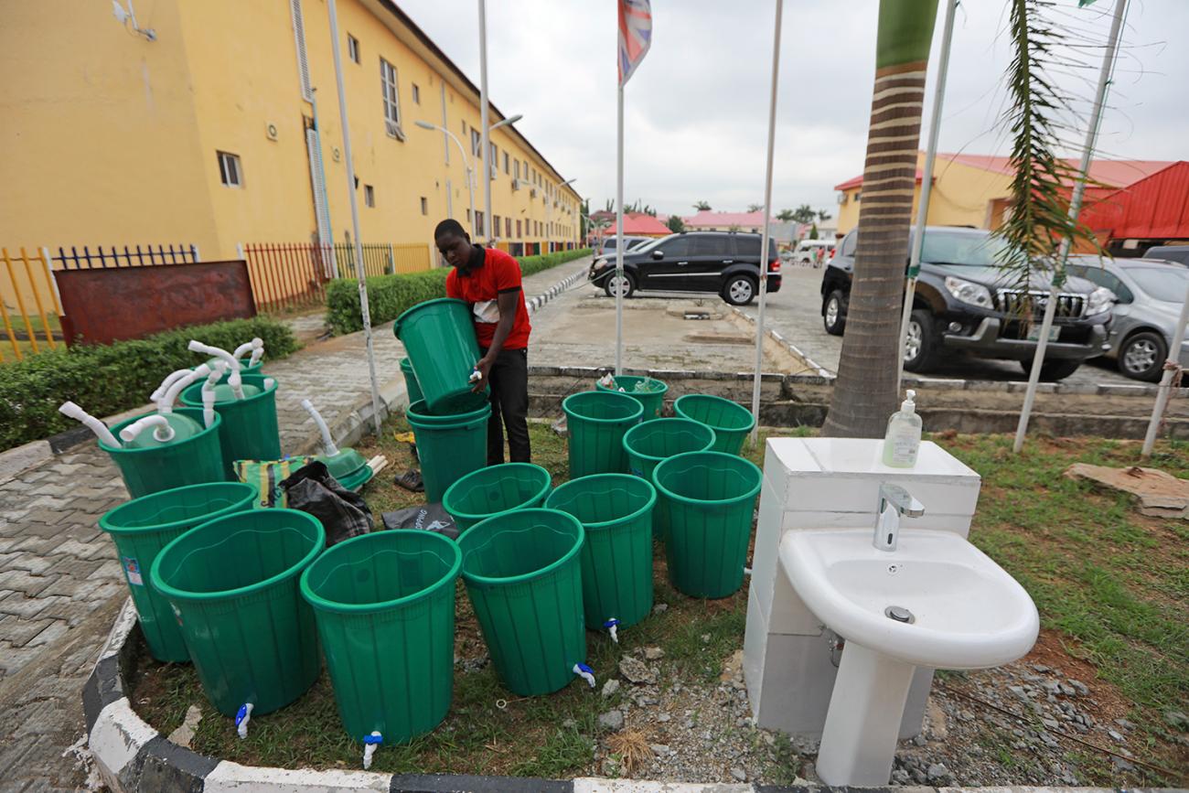 The photo shows a man arranging dark green buckets next to a standing sink basin in an outdoor area. 