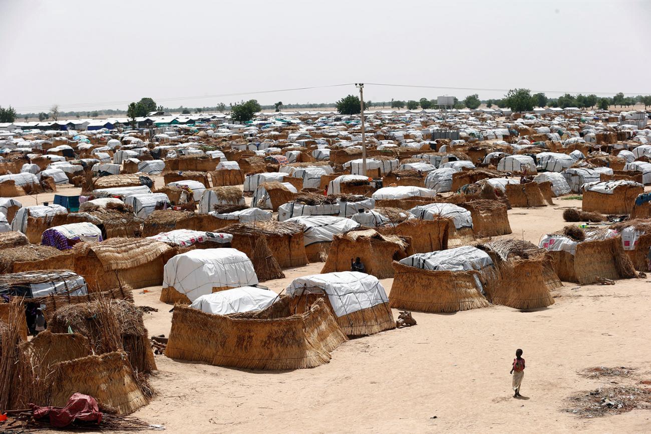 The photo shows a small girl in the foreground against the backdrop of a massive camp.