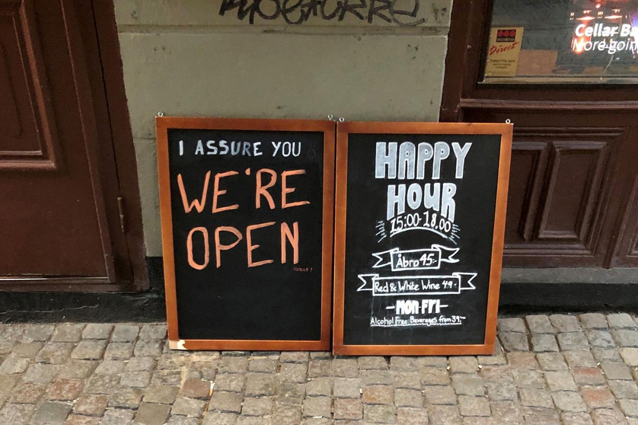 The photo shows a chalk sign in front of a bar that reads, "We're Open."