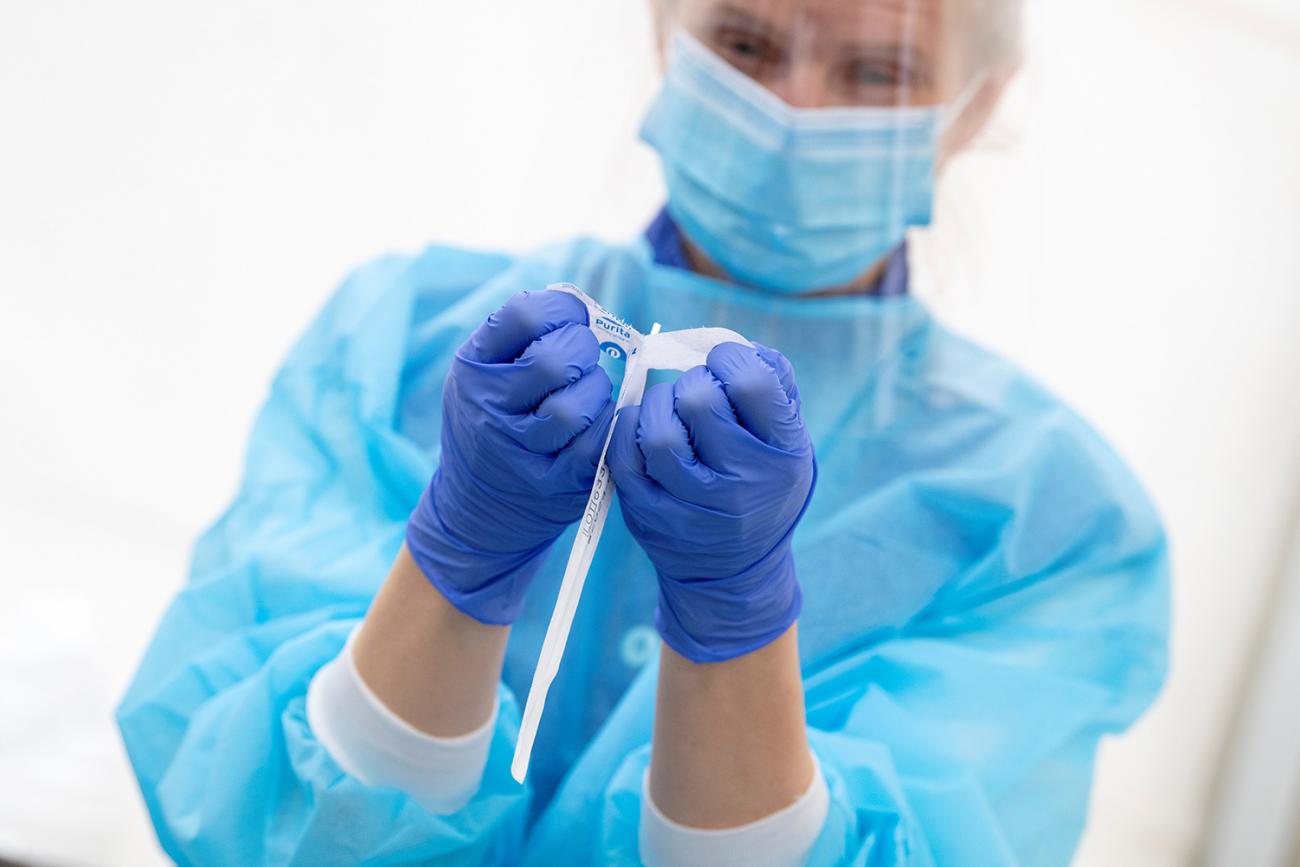 The photo shows a health worker in blue protective gear opening a sterile package.