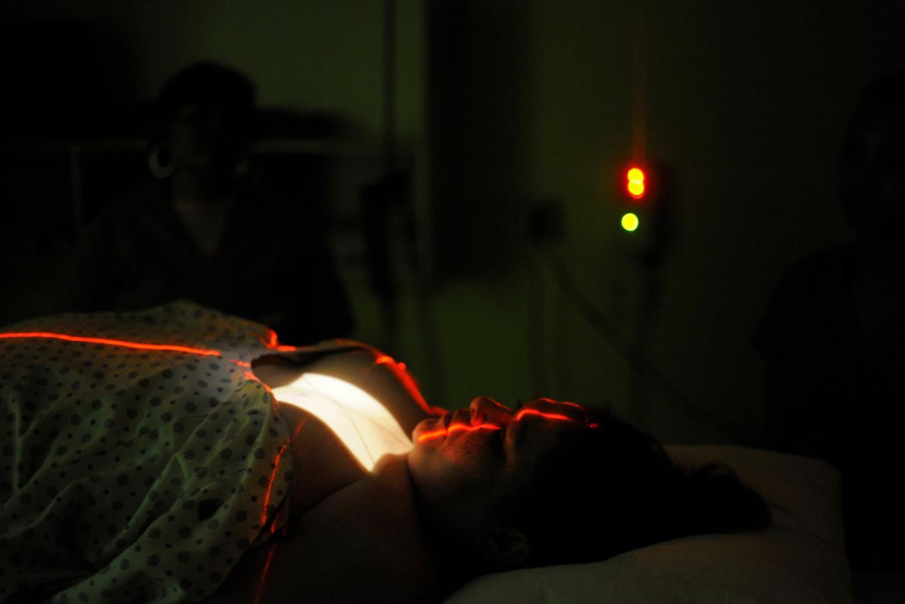 The photo shows a woman in a dark room lying down on a table with red lights on her.