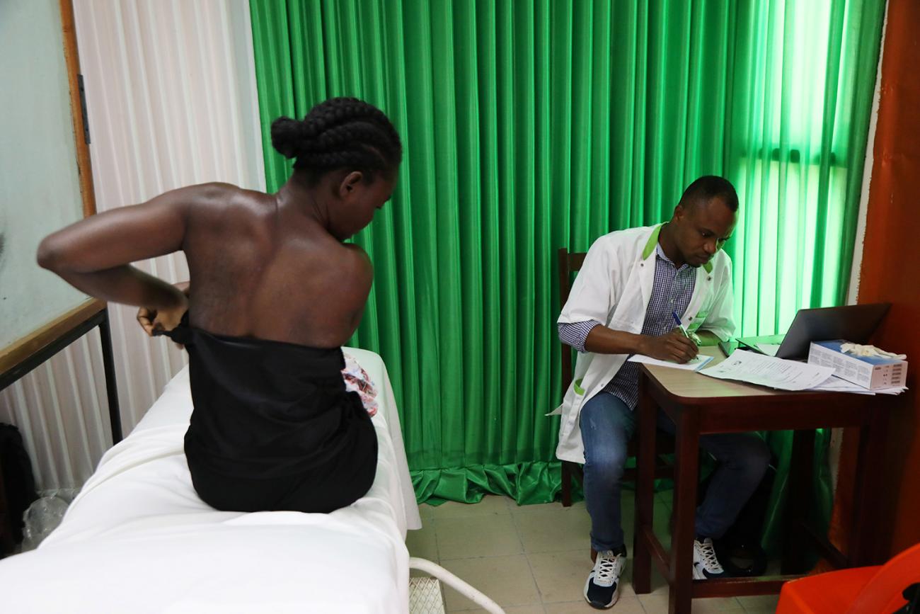 The photo shows the woman on a bed while a doctor sits in a chair next to her. She is in the process of undressing. 