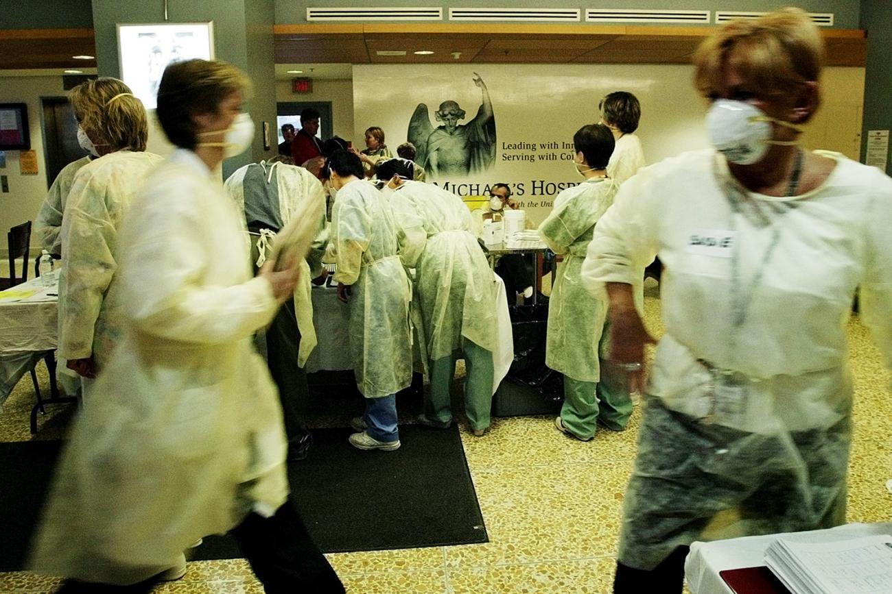 The photo shows a bustle of hospital staff moving around the waiting area of a hospital, whose namesake is the subject of a mural in the background, behind the information desk.