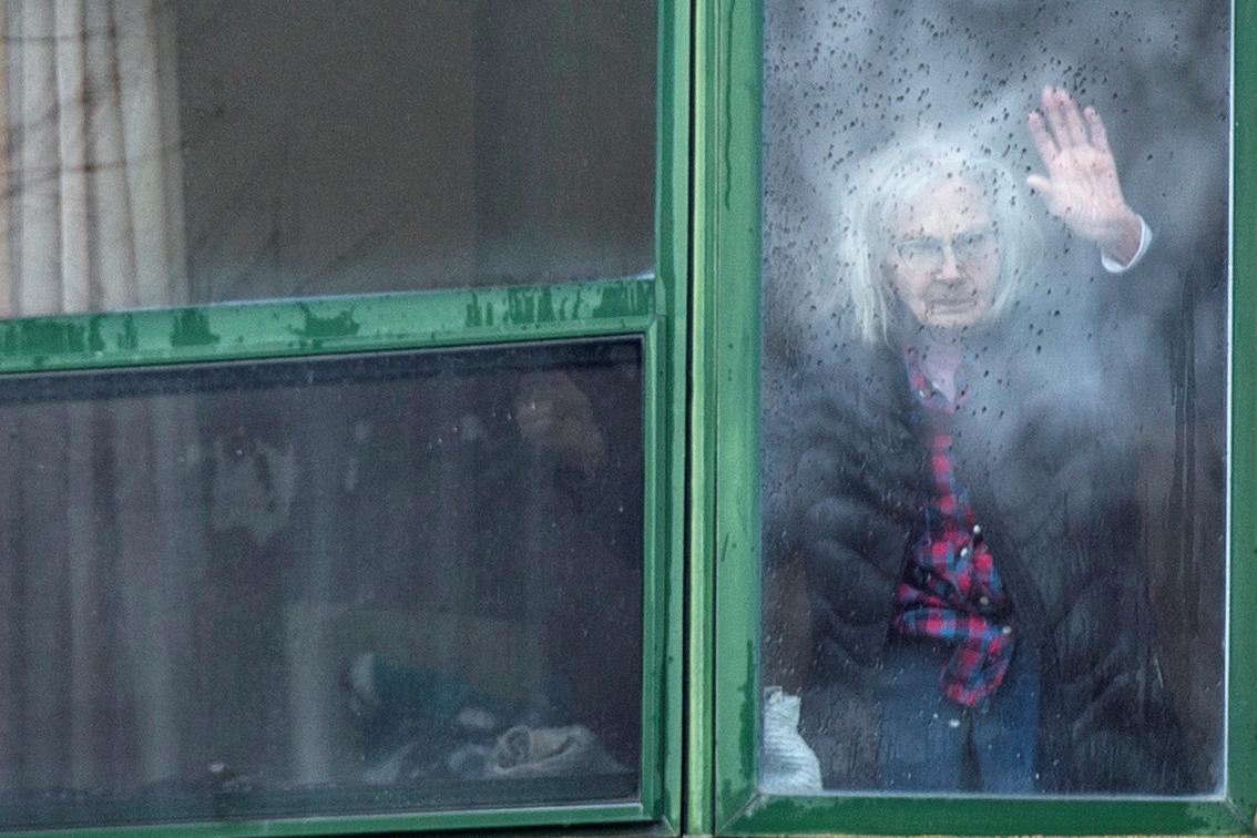 The photo shows the older resident waving through the rain-splattered window appointed with green slats. 