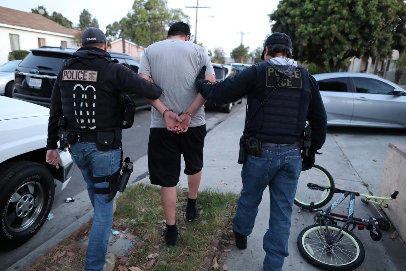 The photo shows two officers leading a person away from the camera in handcuffs. 