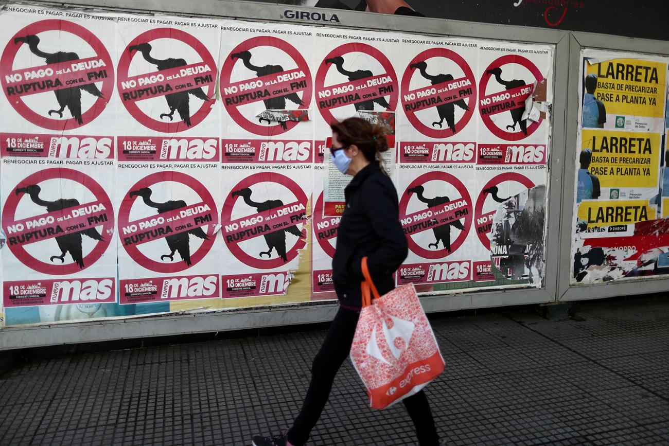 The photo shows a woman walking past a wall on which are plastered dozens of political banners. 