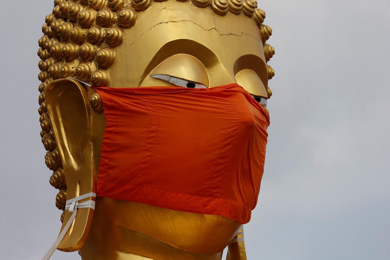 The image shows a golden headed Buddha wearing a bright red mask. 