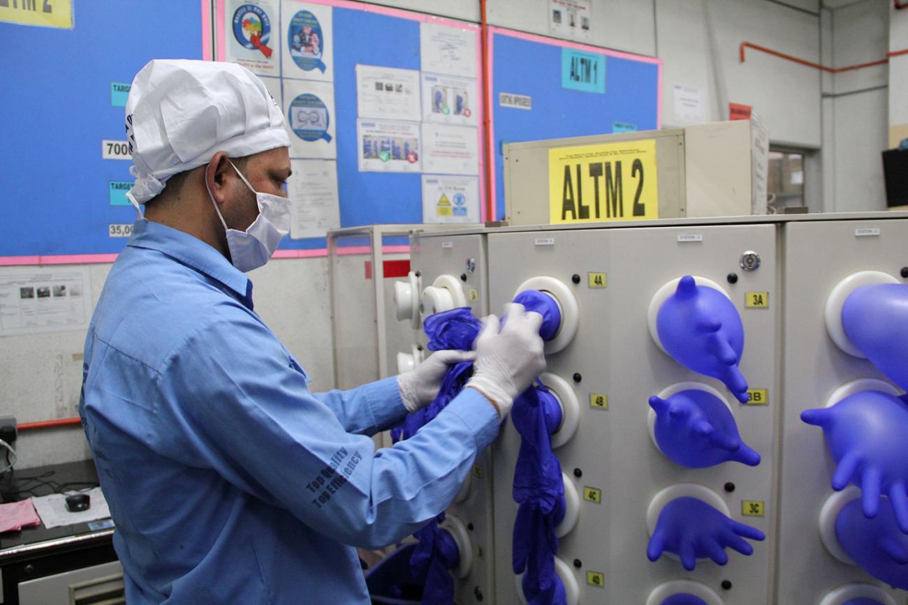 Picture shows the worker stretching gloves over nozzles that inflate them. 