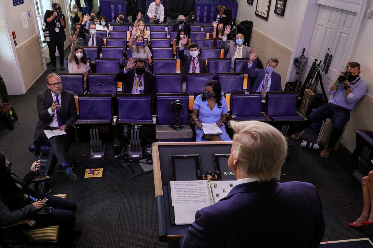 The photo shows the president from behind as he stands at the podium and listens to the reporter in a sparse press briefing room.
