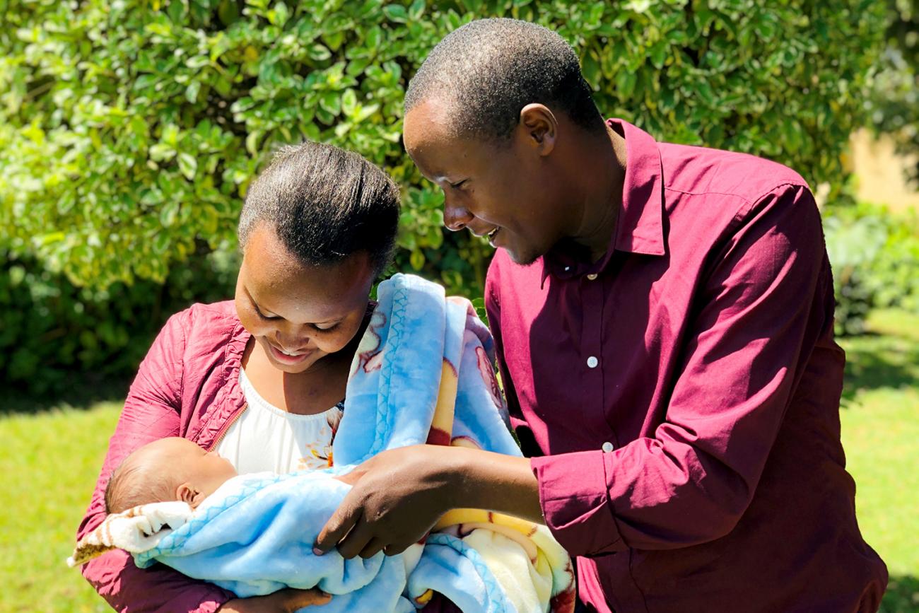 Picture shows a couple holding their newborn baby outside. 