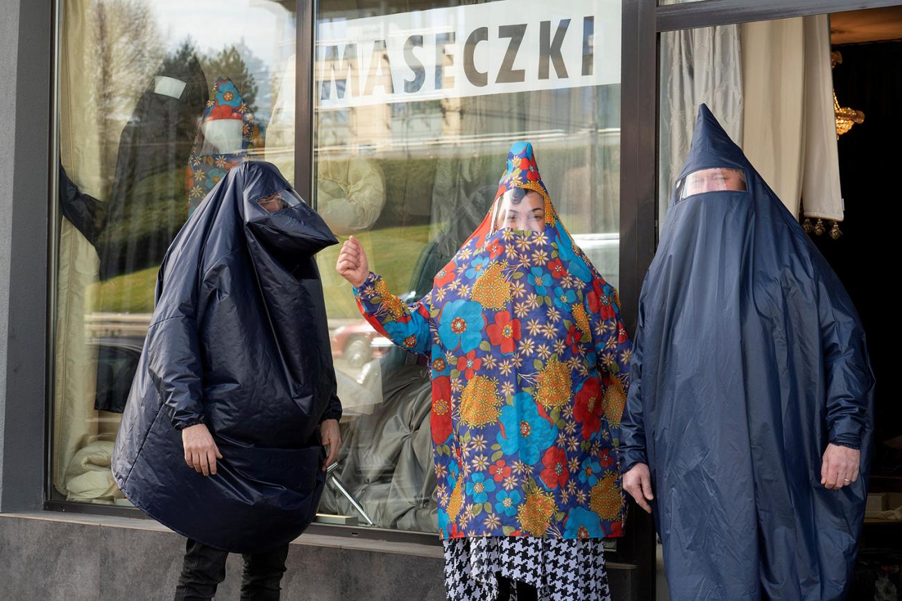 Picture taken shows three people with crazy body coverings on in front of a store. 