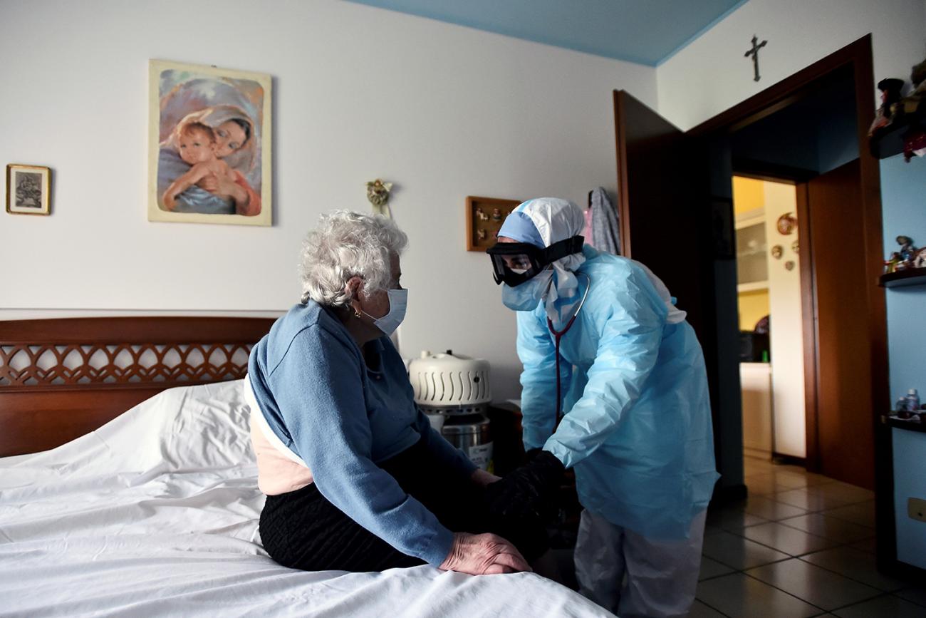 The photo shows a health worker leaning over a person sitting on a bed. REUTERS/Flavio Lo Scalzo