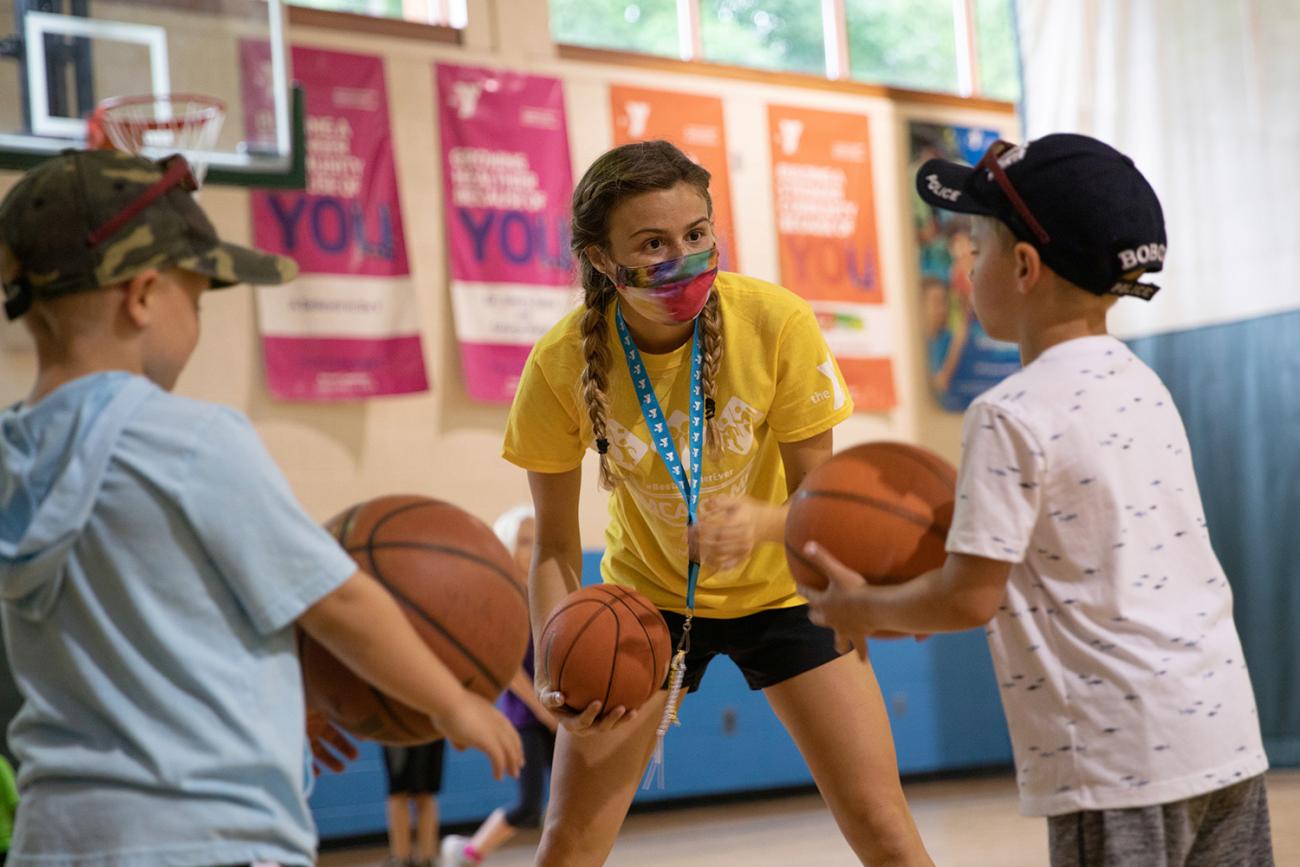 The photo shows the counselor leaning down to interact with the little unmasked kids.
