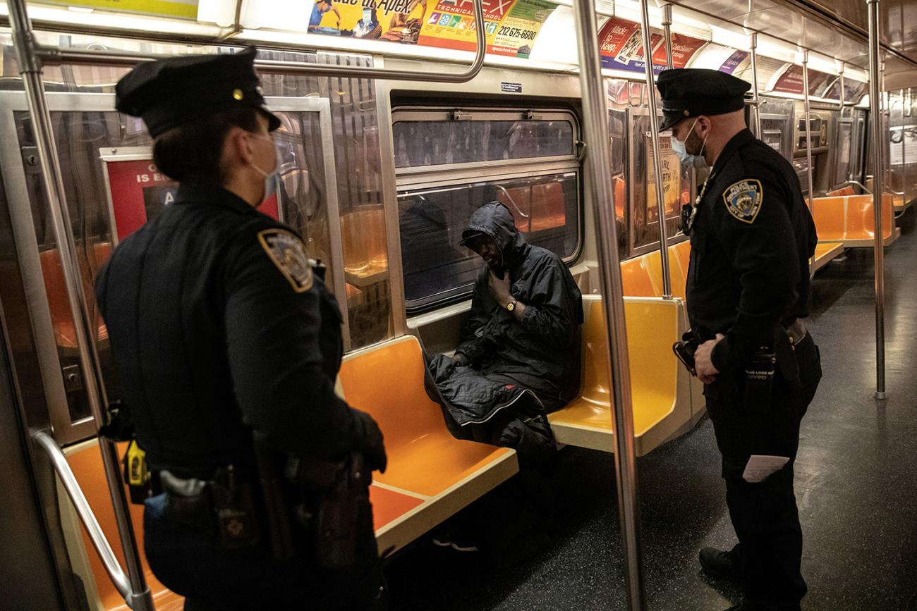 The photo shows two uniformed officers in masks confronting a man sacked out in an otherwise empty subway car. 