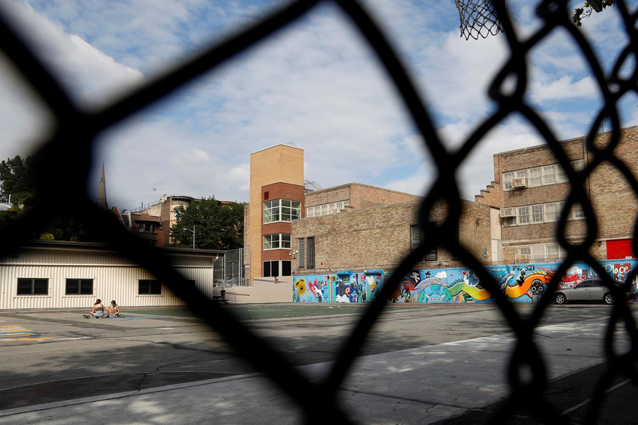 The photo shows an almost empty playground on a sunny day through a chain-link fence. 