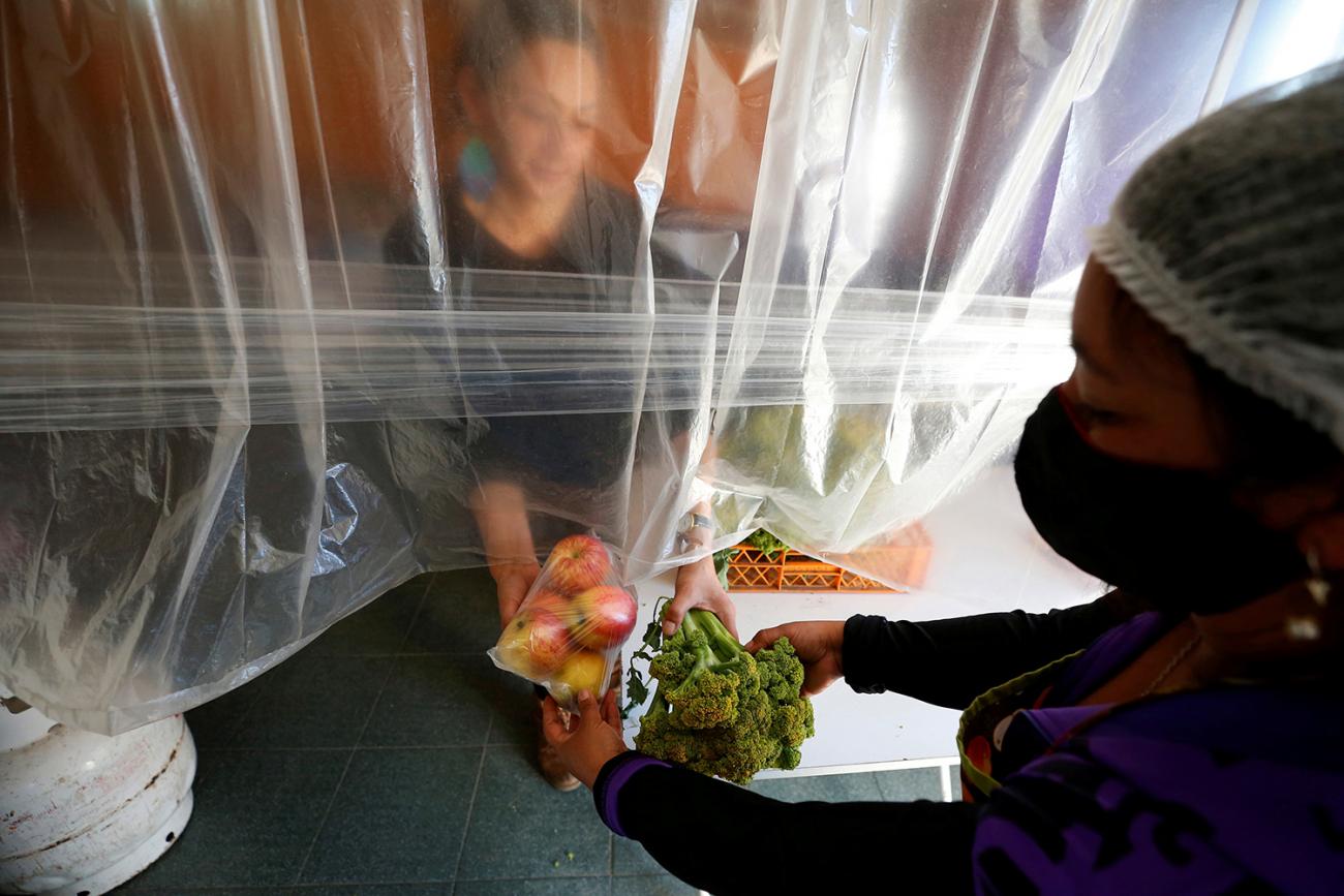 The photo shows a worker haninng food to a person through plastic sheeting. 