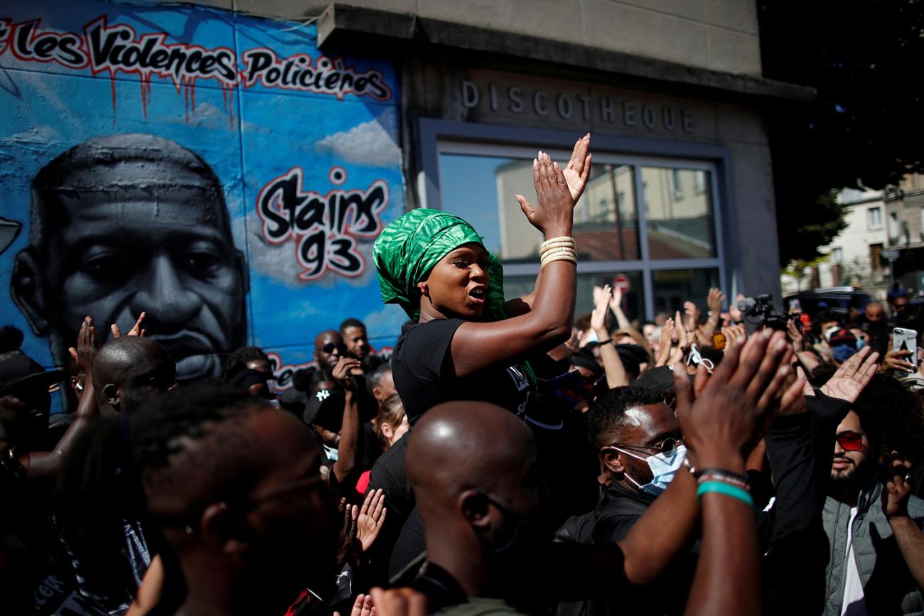 The photo shows Assa standing above a crowd clapping while many people in the crowd have upraised hands, also clapping. 