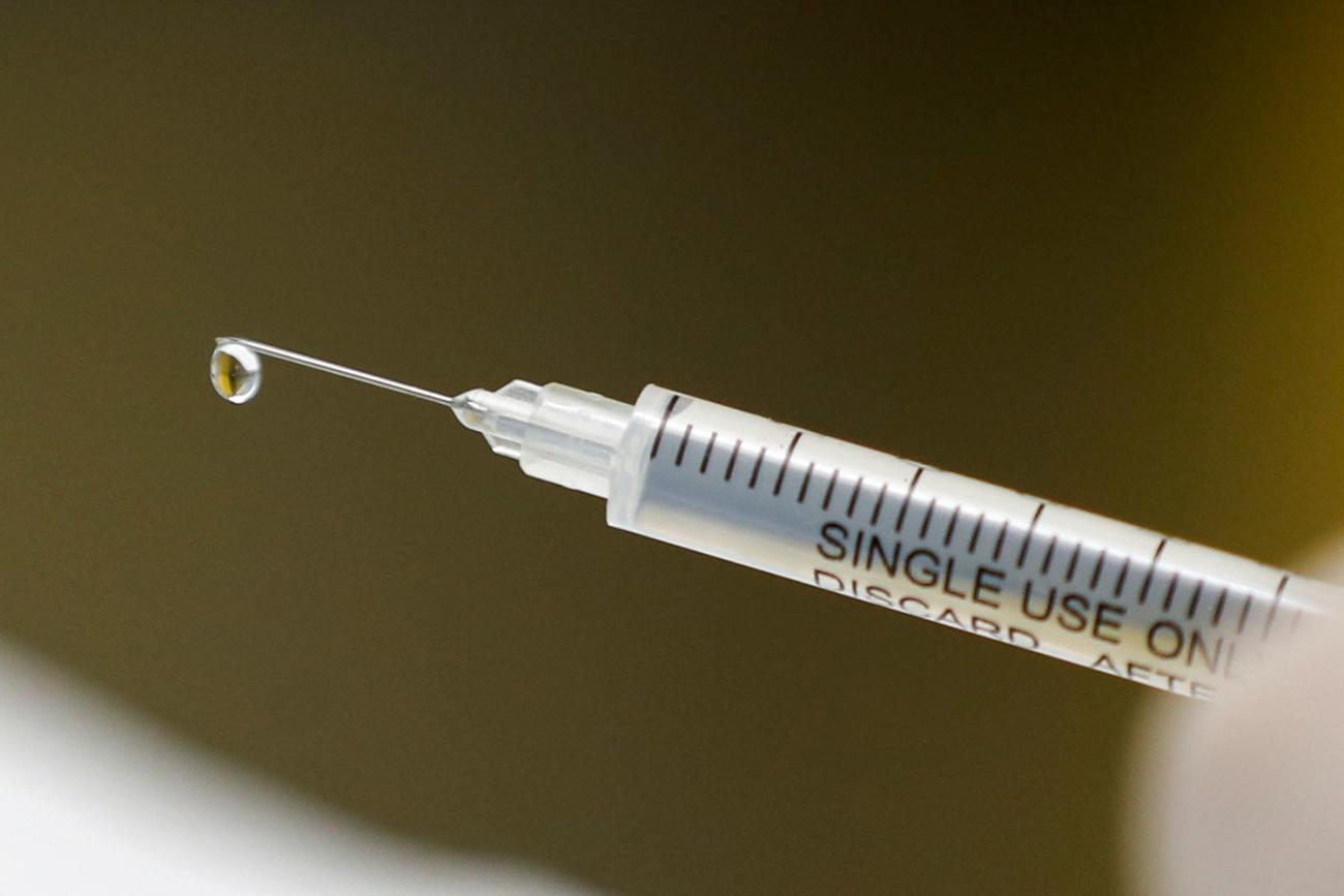 Picture shows a syringe with a single drop of clear liquid forming at the tip of the needle. 