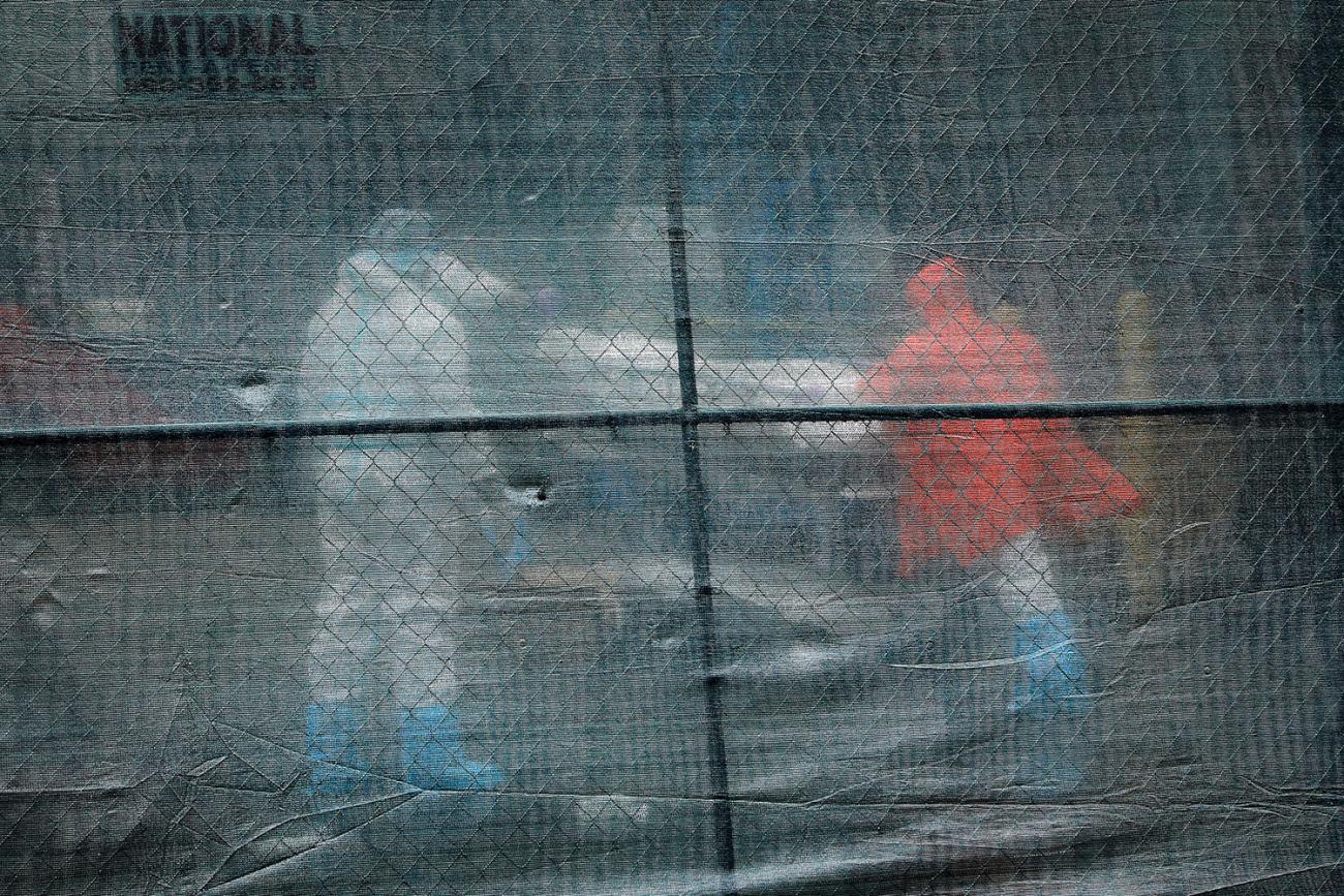 The photo shows a number of health workers moving a body from behind a fence. 