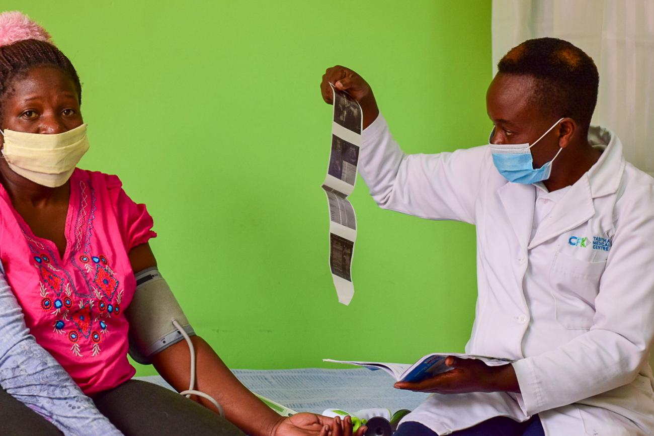 The photo shows the woman with a blood pressure cuff on her arm sitting on a hospital bed with  b right green wall in the background. A doctor sits next to her holding what appears to be a series of ultrasound shots of a fetus. OPTIONS/Meshack Acholla