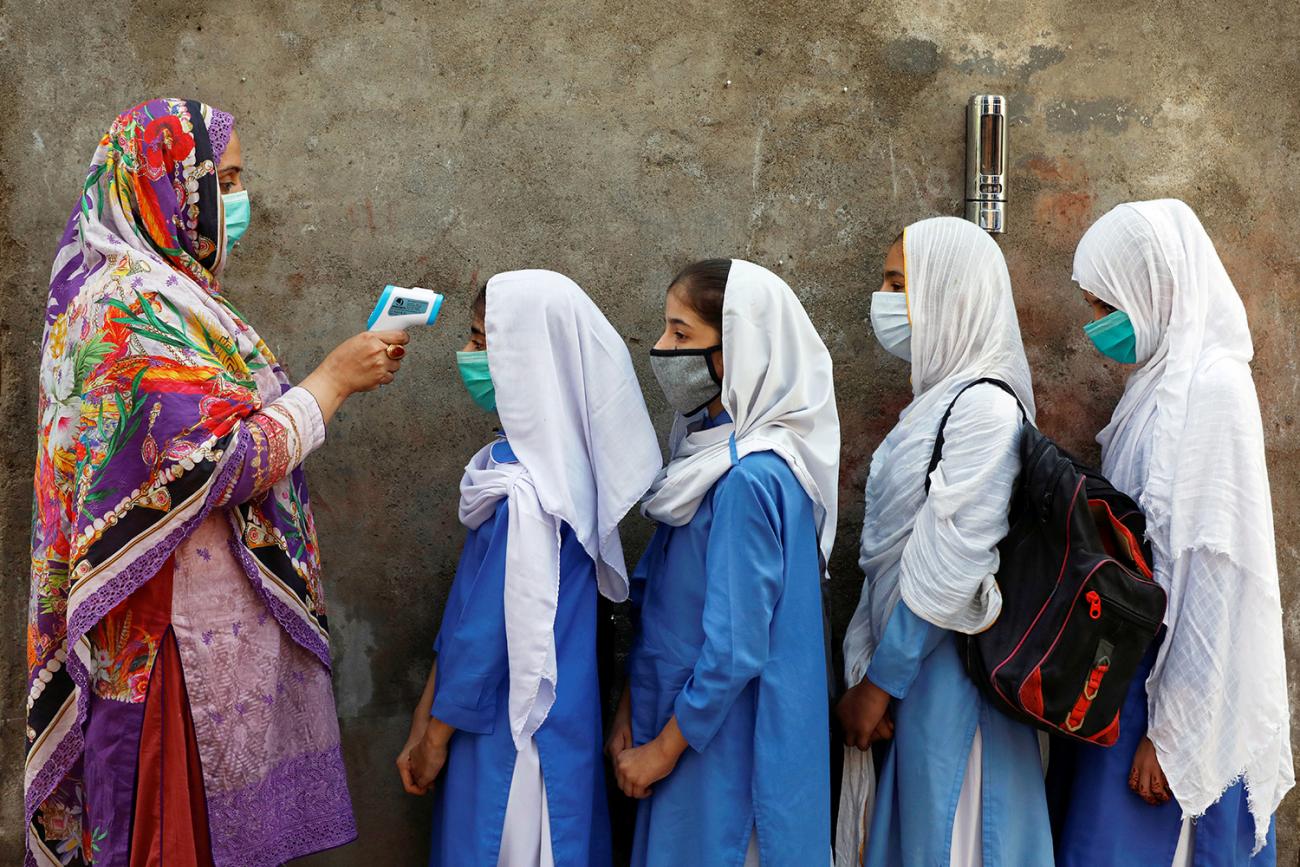 The photo shows a line of girls facing a woman holding a thermometer gun. 