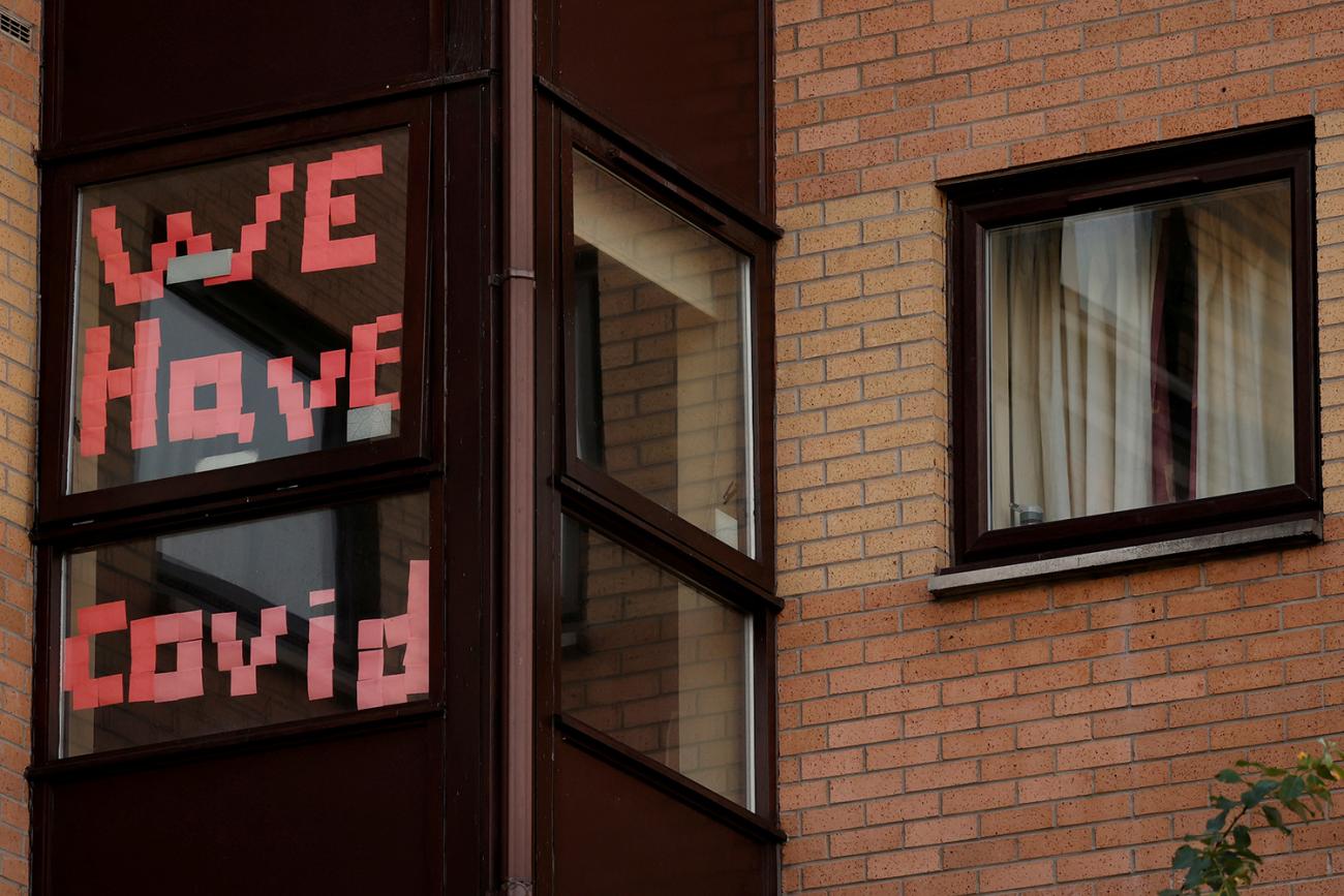 The photo shows a brick dormitory-style building with the words "We Have Covid" written in the window. 