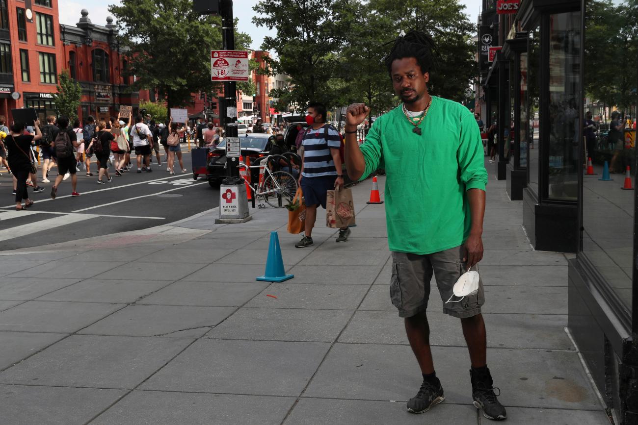 The photo show Garrett wearing a bright green shirt standing in front of a store with his fist raised. 