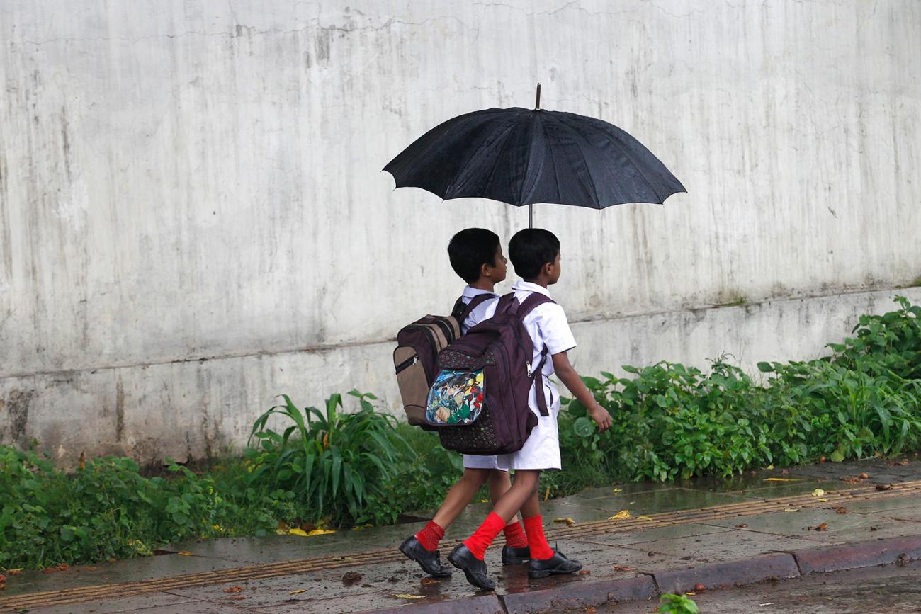 The photo shows two small children with umbrellas walking through the rain. 