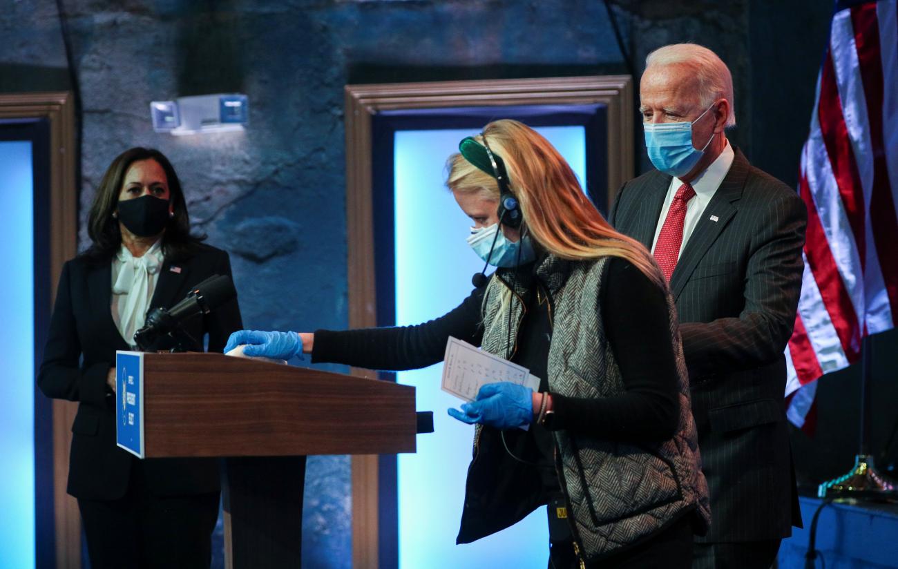 Vice President-elect Senator Kamala Harris and U.S. President-elect Joseph R. Biden watch as an aide sanitizes the podium as Biden prepares to speak to reporters in Delaware on November 19, 2020.