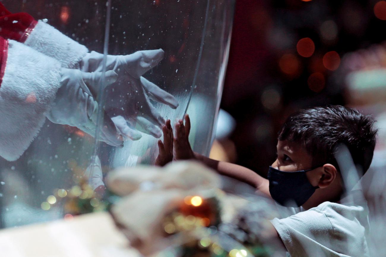 A man dressed as a Santa Claus inside a plastic bubble, greets a child in a shopping mall amid the coronavirus disease outbreak in Brasilia, Brazil on December 15, 2020. 