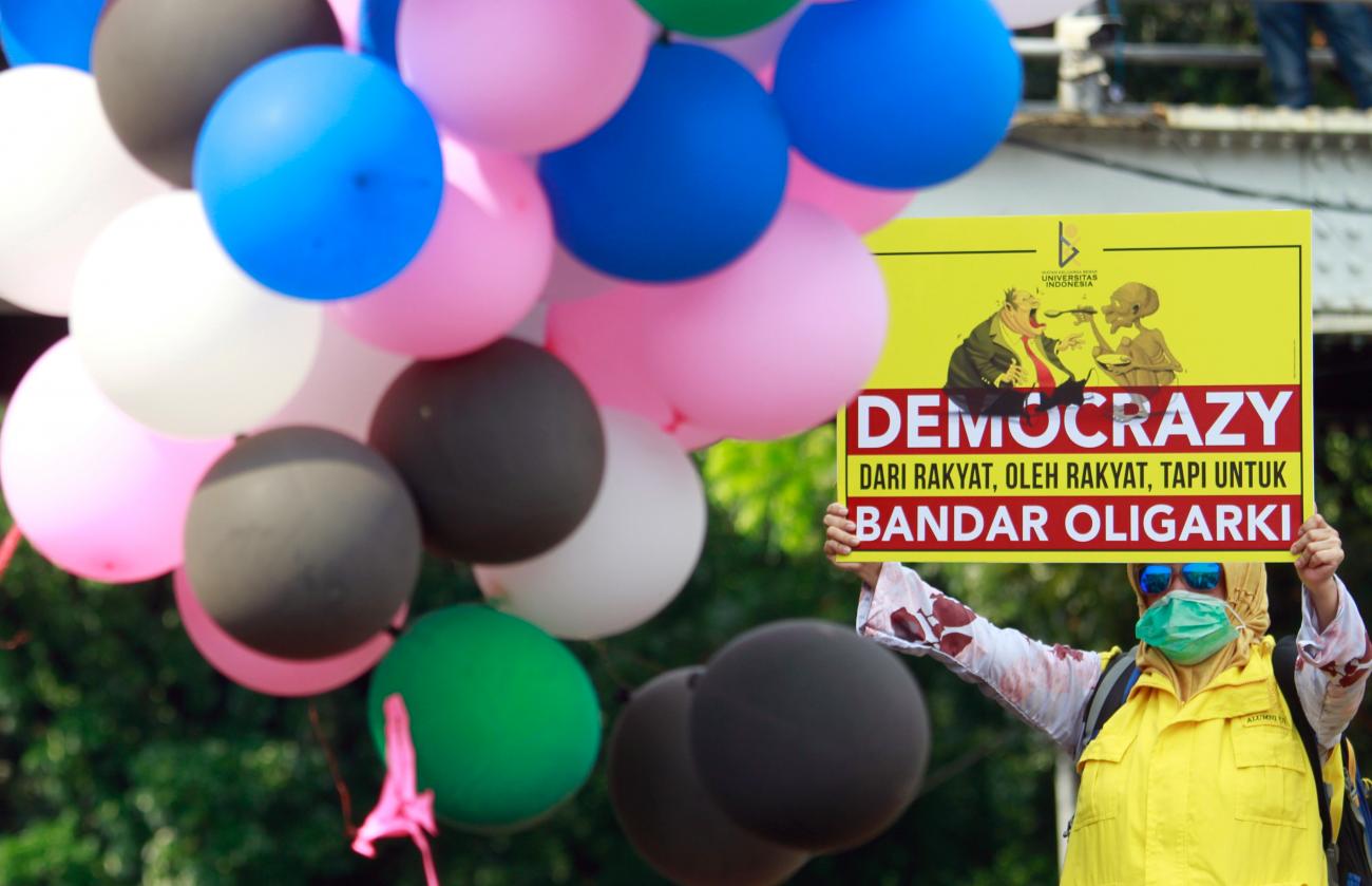 A member of Indonesian trade unions holds a banner during protest against the government's labor reforms in a "jobs creation" bill, in Indonesia on October 28, 2020. The banner reads: "Democrazy from the people by the people for oligarchic".