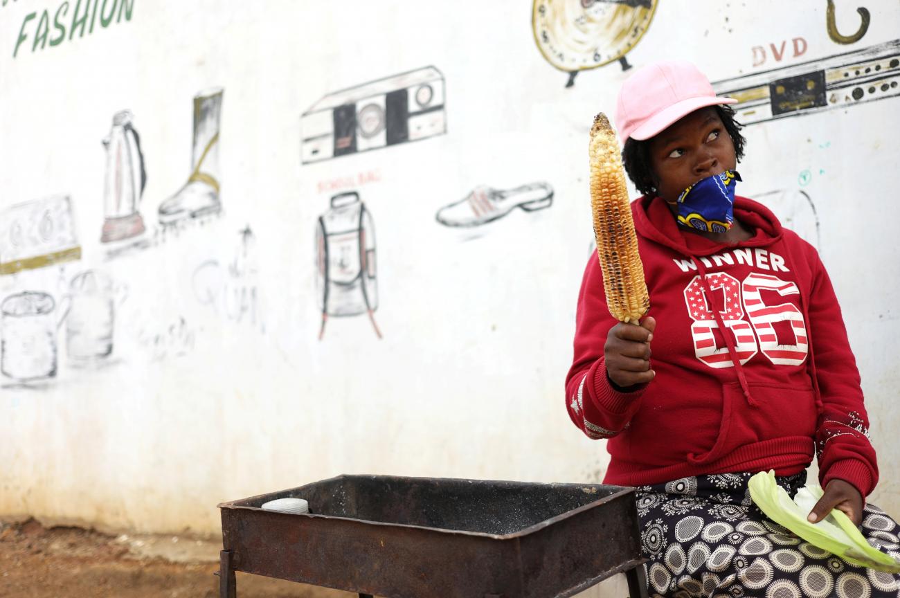 A woman wearing a mask holds a corn cob while chatting to a customer, amid the coronavirus disease pandemic at the the Freedom Park informal settlement in South Africa on December 18, 2020.