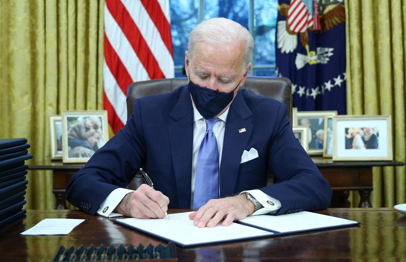 President Joe Biden signs executive orders in the Oval Office of the White House in Washington, including one to halt the U.S. withdrawal from the WHO in Washington, DC on January 20, 2021.