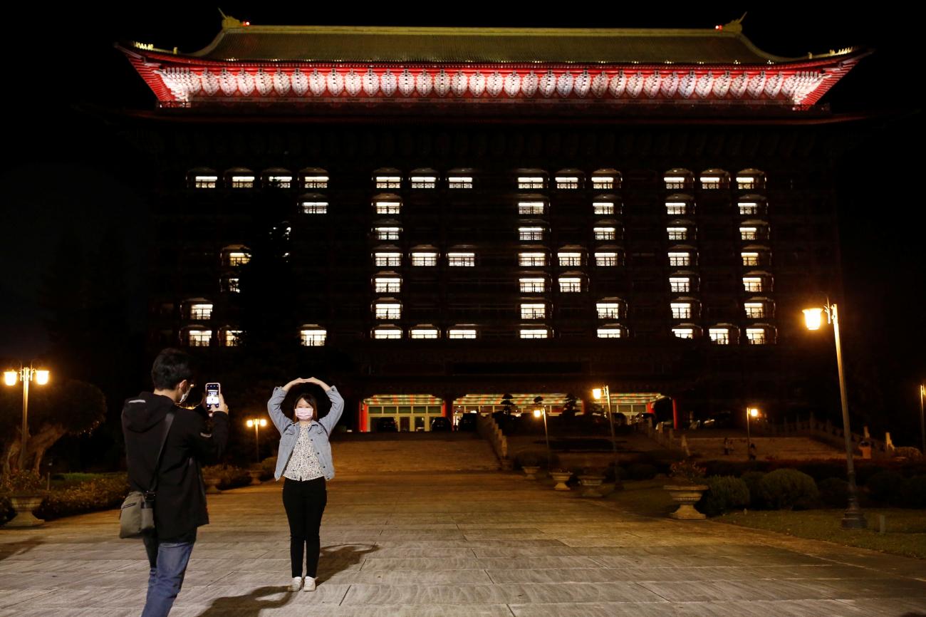 People wearing a face masks pose in front of the Grand Hotel that's using hotel room lights to celebrate zero confirmed cases in Taipei, Taiwan on April 16, 2020.