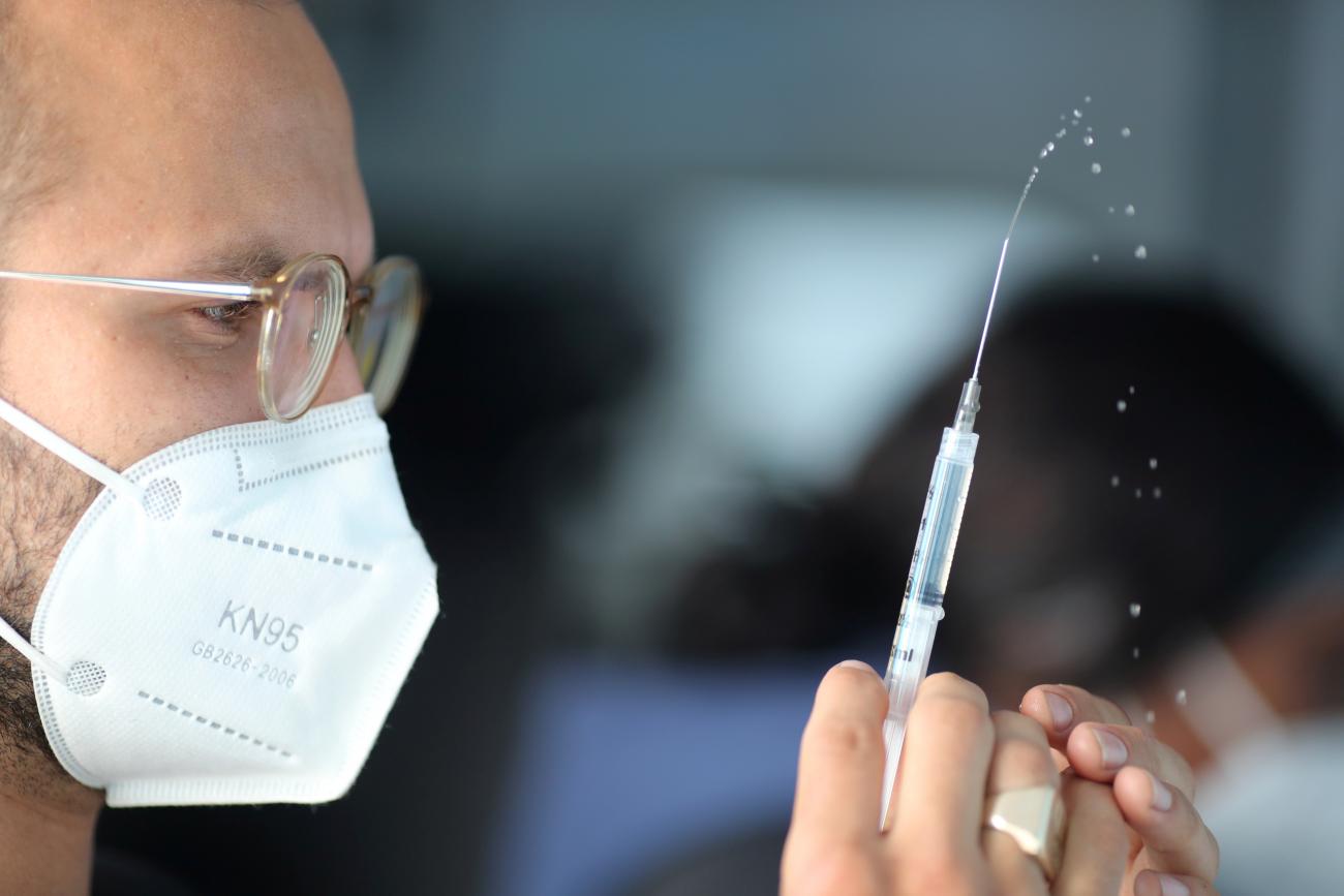An EMT squirts saline solution before preparing a Pfizer vaccine at a mobile vaccination drive in Los Angeles, California on March 17, 2021.
