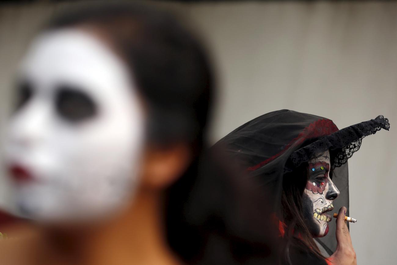 A woman, painted to look like the popular Mexican figure “Catrina”—a character also known as "The Elegant Death”—smokes a cigarette at the annual Catrina Fest in Mexico City on November 1, 2015.