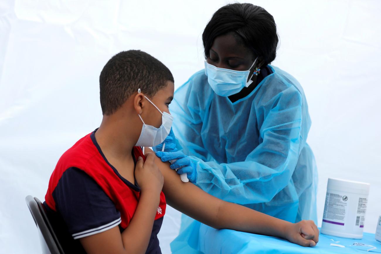 12-year-old Justing Concepcion receives a dose of the Pfizer-BioNTech vaccine from a registered nurse, Angela Nyarko, in PPE during a vaccination event for local adolescents and adults outside the Bronx Writing Academy school in New York City.