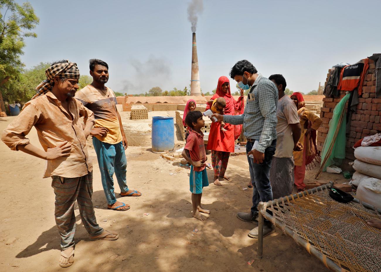A health-care worker checks the temperature of a boy during a COVID-19 vaccination drive at a brick kiln at Kavitha village on the outskirts of Ahmedabad, India on April 8, 2021. 