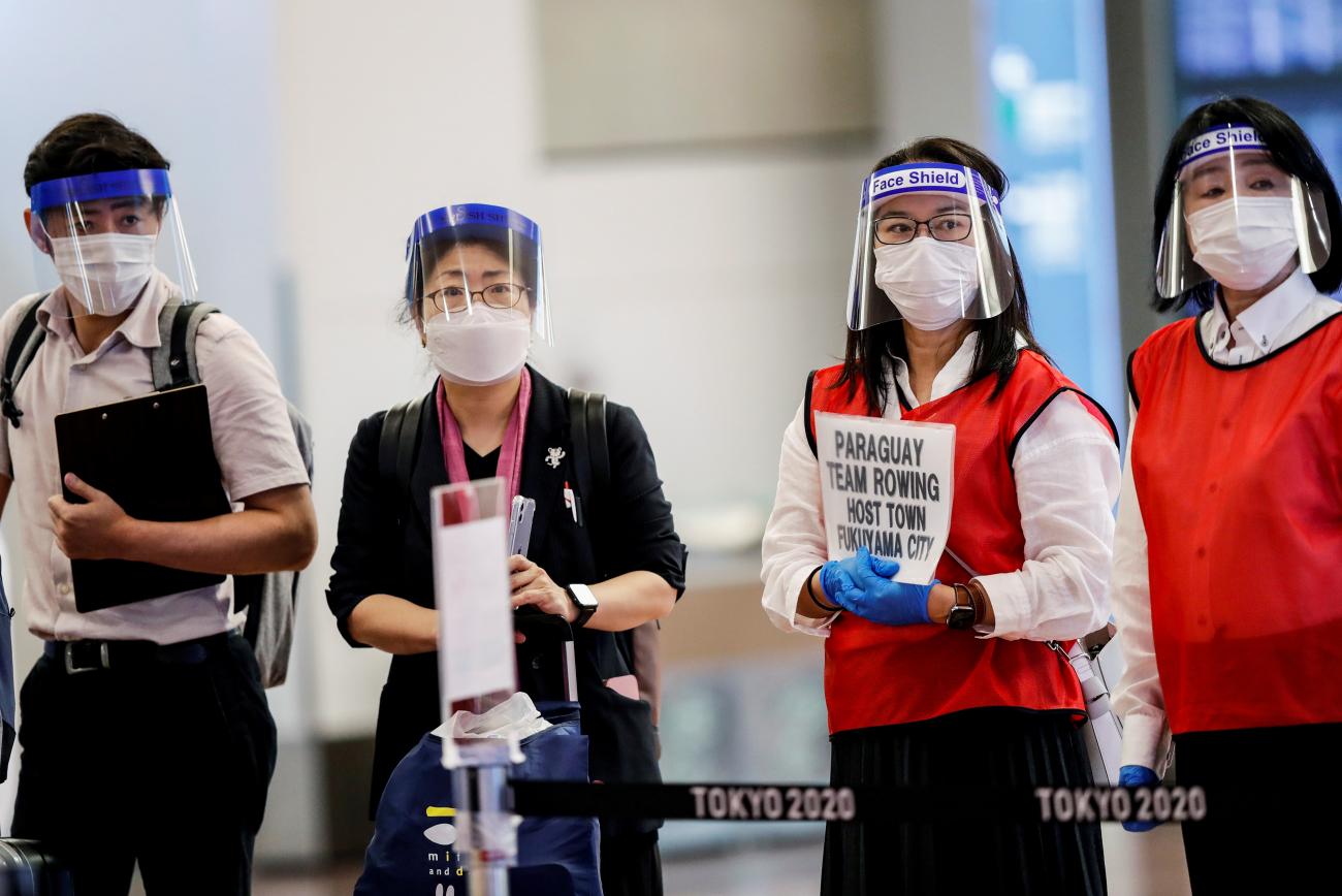 Four staff members wear face masks and shields to help prevent COVID-19 wait for athletes to arrive at Haneda Airport before the Olympic Games in Tokyo, Japan on July 8, 2021. 