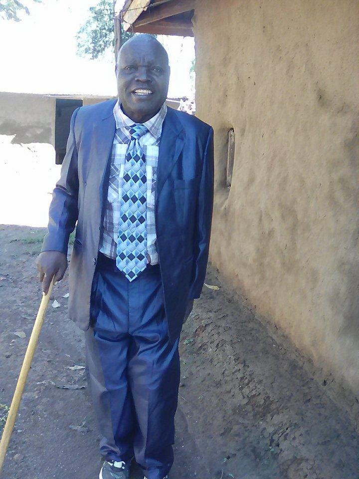 Charles Mushila Shibeka is smiling and wearing a dark blue suit and holding a cane.