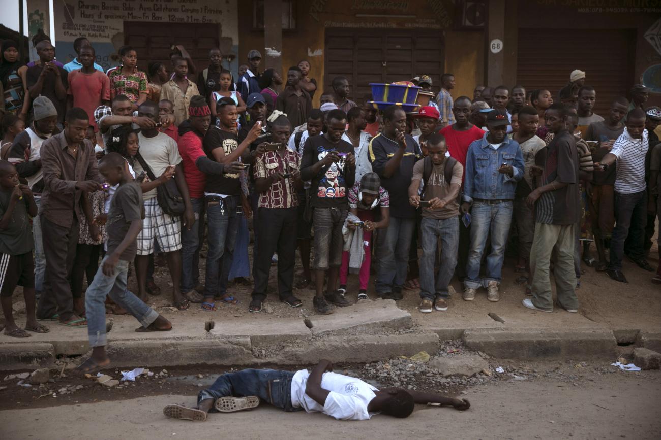 Bystanders stand around the body of a suspected Ebola victim lying in a street in the town of Koidu, Kono district in Eastern Sierra Leone, December 18, 2014. Sierra Leone, neighbouring Guinea and Liberia are at the heart of the world's worst recorded outbreak of Ebola.