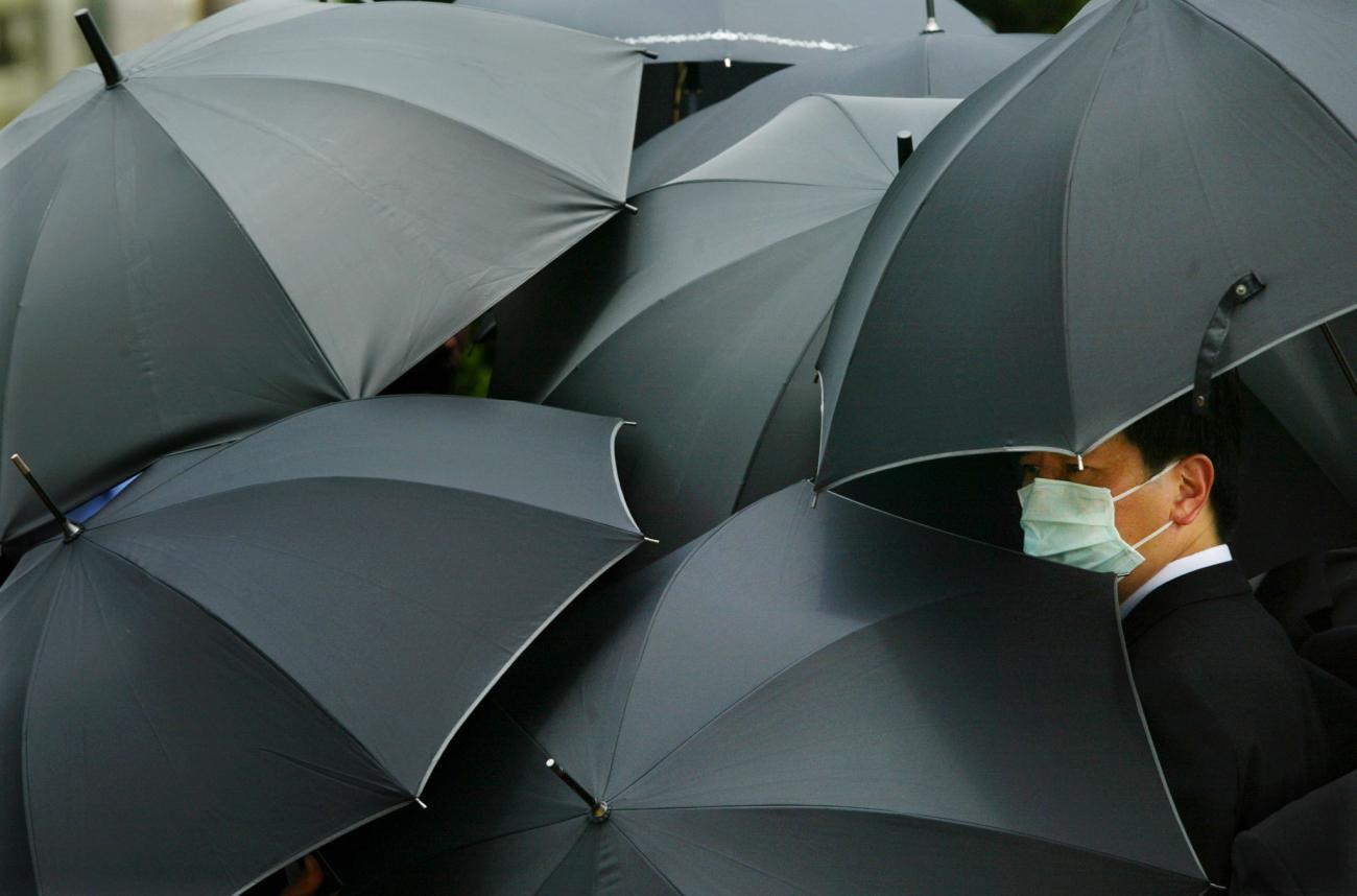 A mourner wearing a mask to ward off SARS hides under an umbrella during the funeral of SARS doctor Tse Yuen-man in Hong Kong May 22, 2003. Tse, the first front-line doctor to be killed by the disease in the territory