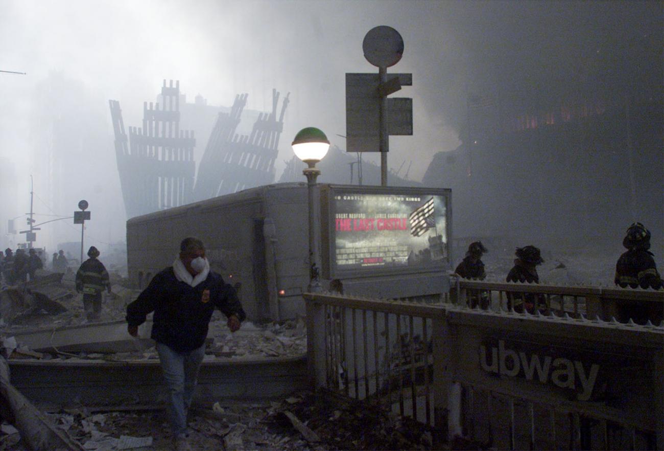 The wreck of the World Trade Center smolders in the background as a man passes a subway stop after two planes crashed into each of the twin towers in New York ,on September 11, 2001.