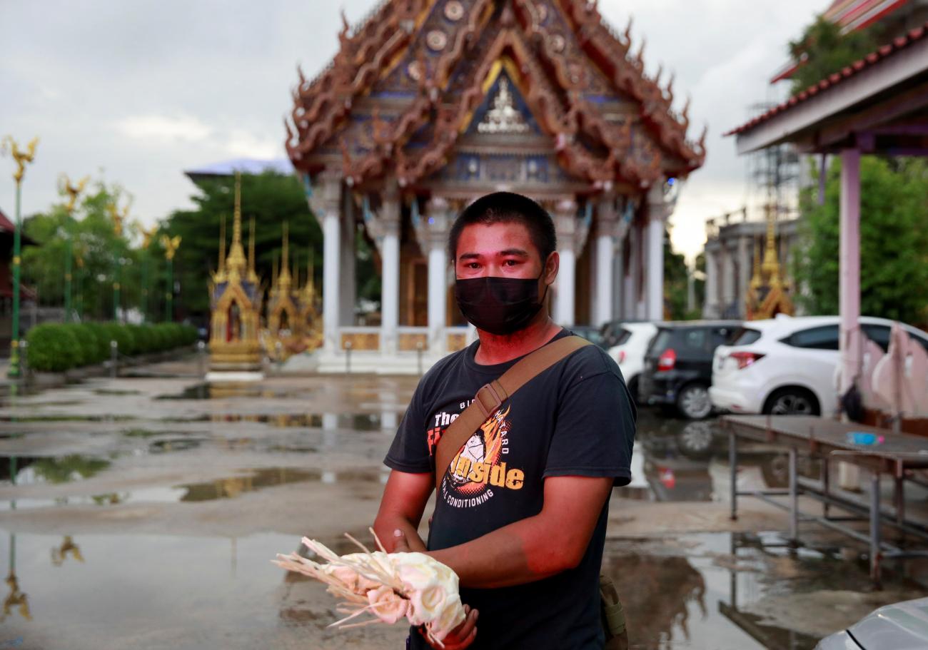 A man holds flowers as he waits for the funeral of his wife who died from coronavirus disease when she was 8 months pregnant, standing in front of a temple in Bangkok, Thailand, on August 5, 2021.