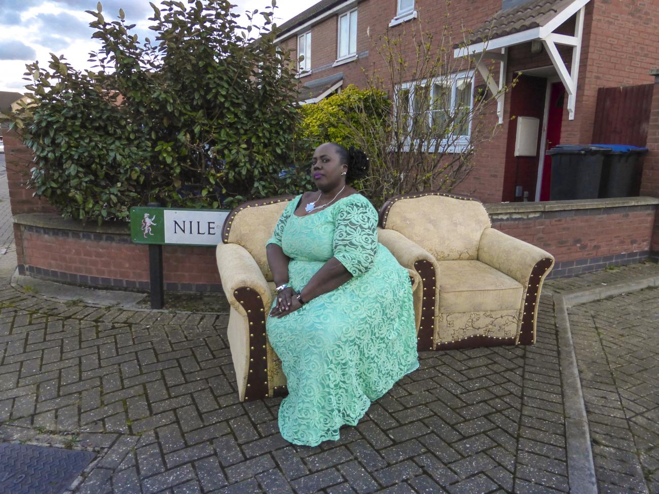 A woman sits in a green gown on a couch outside